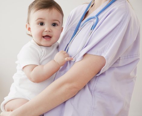 Smiling baby held by a healthcare professional wearing a stethoscope.