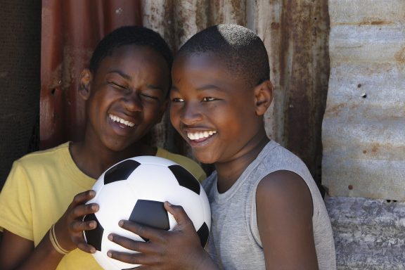 Two joyful children holding a football, smiling at each other.